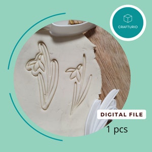 May include: A close-up of two white plastic cookie cutters shaped like snowdrop flowers. The cutters are on a white surface with a brown background. DIGITAL FILE 1 pcs