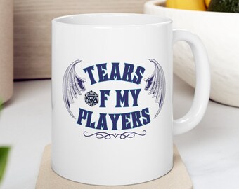 Op de afbeelding: Witte keramische mok met een blauw en grijs ontwerp. De mok heeft een 20-zijdige dobbelsteen met vleugels en de tekst "Tears of My Players".
