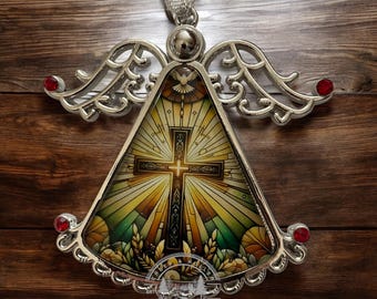 May include: Silver angel ornament with a stained glass design featuring a cross and a dove. The ornament has red jewels on the wings and a gold background.