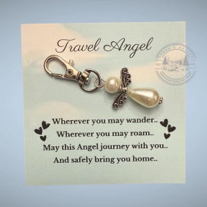 May include: A Travel Angel keychain with a pearl-like body and silver-tone wings and accents. The keychain is attached to a card with the text "Travel Angel" and a poem about safe travels.