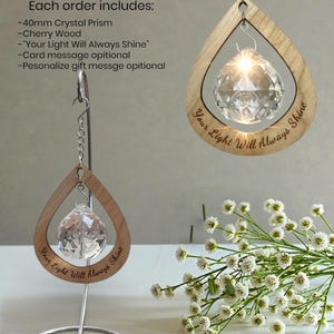 May include: A crystal prism ornament with a cherry wood frame, available with a tabletop stand or hanging chain. The frame is teardrop-shaped and engraved with the words "Your Light Will Always Shine". The prism is approximately 40mm in diameter.