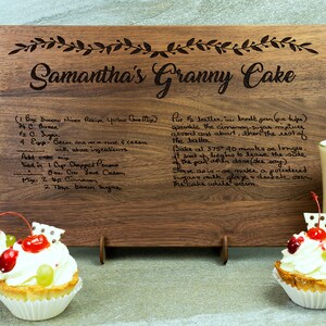 K&ouml;nnte beinhalten: Ein Holzbrett zum Schneiden mit der Aufschrift "Samantha's Granny Cake" und einem handgeschriebenen Rezept f&uuml;r einen Kuchen. Das Rezept enth&auml;lt Zutaten wie Butter, Zucker, Eier und Pekann&uuml;sse. Das Brett ist braun und hat eine nat&uuml;rliche Holzmaserung.