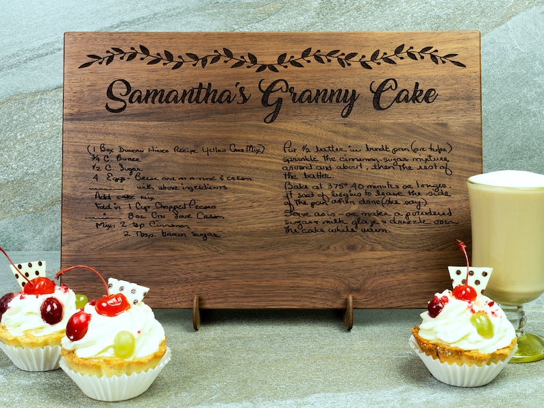 K&ouml;nnte beinhalten: Ein Holzbrett zum Schneiden mit der Aufschrift "Samantha's Granny Cake" und einem handgeschriebenen Rezept f&uuml;r einen Kuchen. Das Rezept enth&auml;lt Zutaten wie Butter, Zucker, Eier und Pekann&uuml;sse. Das Brett ist braun und hat eine nat&uuml;rliche Holzmaserung.