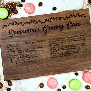 K&ouml;nnte beinhalten: Ein Schneidebrett aus Holz mit dem eingravierten Text "Samantha's Granny Cake". Das Brett enth&auml;lt auch ein handgeschriebenes Rezept f&uuml;r einen gelben Kuchen.