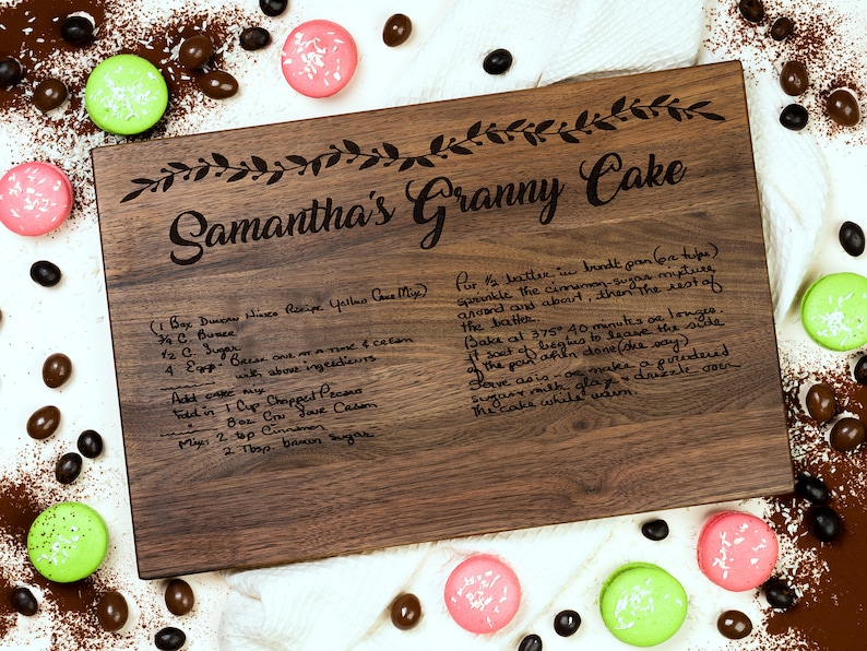 K&ouml;nnte beinhalten: Ein Schneidebrett aus Holz mit dem eingravierten Text "Samantha's Granny Cake". Das Brett enth&auml;lt auch ein handgeschriebenes Rezept f&uuml;r einen gelben Kuchen.