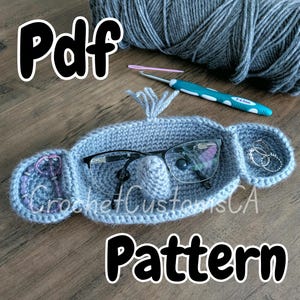 May include: A gray crocheted glasses holder shaped like an elephant with a small pocket for jewelry. The text "Pdf Pattern" is written below the holder.