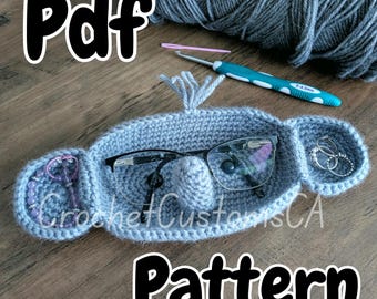 May include: A gray crocheted glasses holder shaped like an elephant with a small pocket for jewelry. The text "Pdf Pattern" is written below the holder.