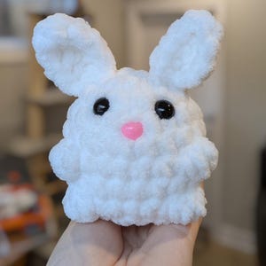 May include: A white crocheted bunny plush toy with black eyes and a pink nose.