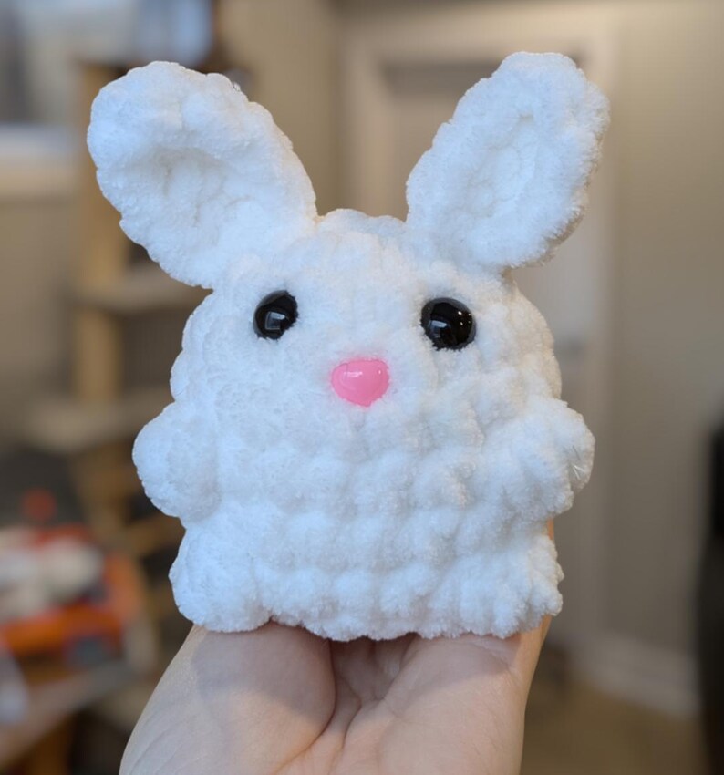 May include: A white crocheted bunny plush toy with black eyes and a pink nose.