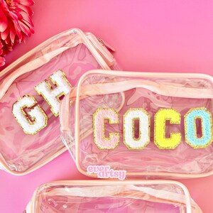 Puede incluir: Tres bolsas transparentes de plástico con cremallera y ribete rosa. Cada bolsa tiene una letra grande, colorida y esponjosa en la parte delantera. Las letras deletrean "GH", "COCO" y "E".