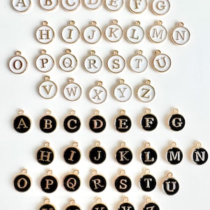 May include: Two sets of gold-toned alphabet letter charms. The first set has white enamel letters on a gold background. The second set has black enamel letters on a gold background.