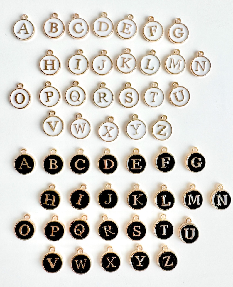 May include: Two sets of gold-toned alphabet letter charms. The first set has white enamel letters on a gold background. The second set has black enamel letters on a gold background.