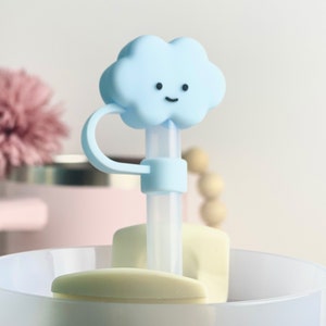 K&ouml;nnte beinhalten: Ein blauer, wolkenf&ouml;rmiger Silikon-Strohhalm-Topper mit einem l&auml;chelnden Gesicht. Der Topper ist an einem durchsichtigen Plastikstrohhalm und einer wei&szlig;en Silikonbasis befestigt.