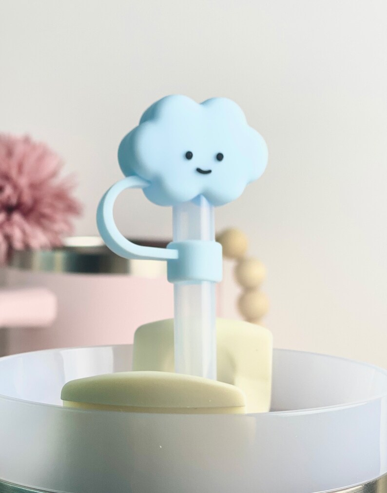 K&ouml;nnte beinhalten: Ein blauer, wolkenf&ouml;rmiger Silikon-Strohhalm-Topper mit einem l&auml;chelnden Gesicht. Der Topper ist an einem durchsichtigen Plastikstrohhalm und einer wei&szlig;en Silikonbasis befestigt.