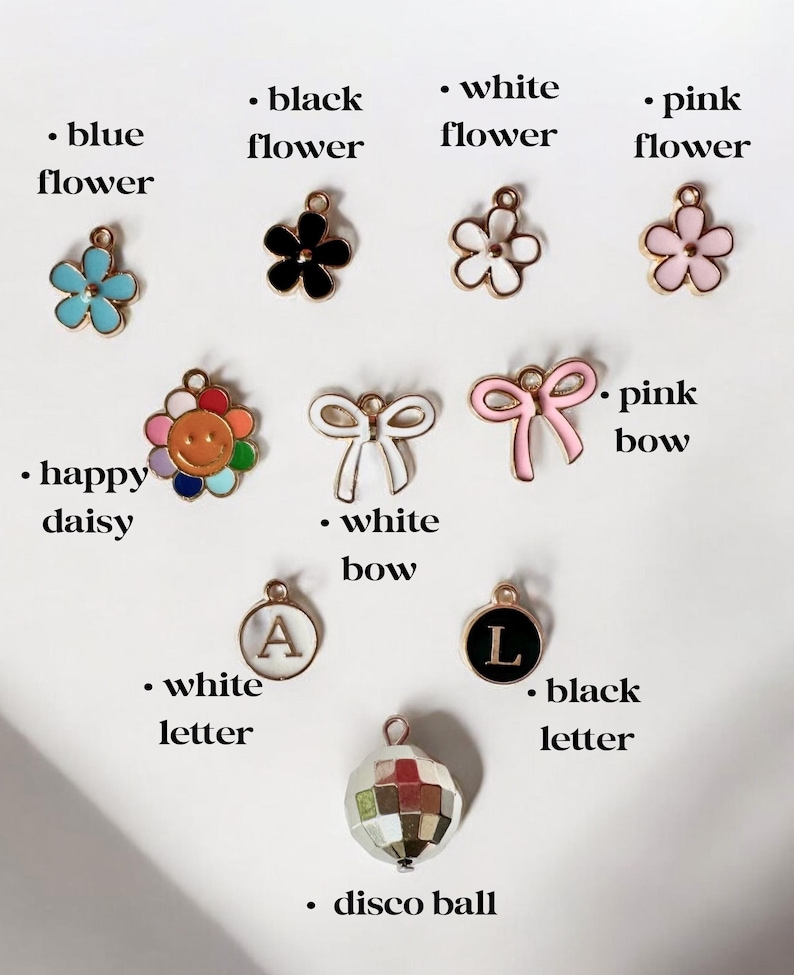 May include: Assortment of colorful charms for jewelry making, including flowers, bows, letters, and a disco ball. The charms are made of metal and have a shiny finish.