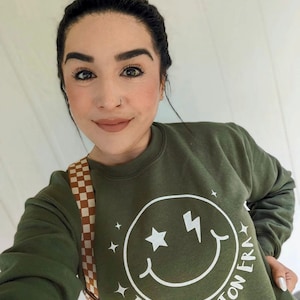 May include: A green sweatshirt with a white smiley face graphic that says "In My Peloton Era".