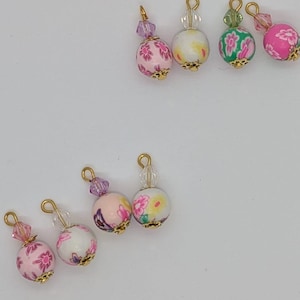 以下が含まれることがあります： 金色のアクセントと透明なクリスタルビーズが付いた、カラフルな花柄のビーズの詰め合わせ。ビーズは金色のワイヤーループに糸で通されています。