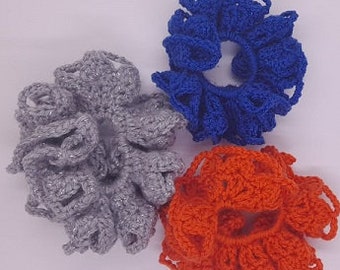 May include: Three crocheted hair scrunchies in grey, orange, and blue. The scrunchies are made with a ruffled design.