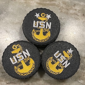 May include: Three black round coasters with a gold anchor and the text "USN" in white. The coasters have a textured surface.