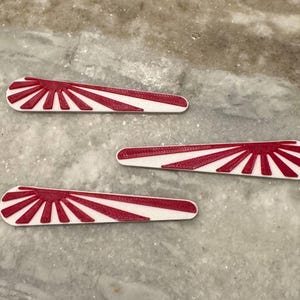 May include: Three white and red plastic ornaments shaped like a rising sun. The ornaments are approximately 5 inches long.