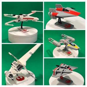 Puede incluir: Una colección de modelos de cazas estelares de Star Wars, incluyendo un X-wing, un Y-wing y un Snowspeeder. Cada modelo está montado en un soporte con el símbolo de la Alianza Rebelde. Los cazas estelares son principalmente blancos, grises y rojos.