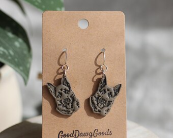 Puede incluir: Un par de pendientes colgantes con una silueta de perro marrón con detalles negros. Los pendientes están en una tarjeta marrón con el texto "Good Dawg Goods" y un gráfico de hueso.