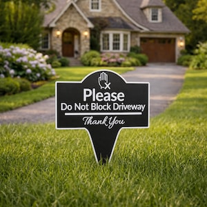 Könnte beinhalten: Ein schwarz-weißes Schild in einem Garten mit der Aufschrift "Please Do Not Block Driveway Thank You". Das Schild hat eine stilisierte Handgrafik und steht vor einem Haus mit Auffahrt und grünem Rasen.