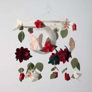 Mobile with light pink butterflies, red roses, burgundy dahlias, and white pink centered cherry blossoms hang off a bamboo hoop with a white crescent moon with three red roses in the middle.