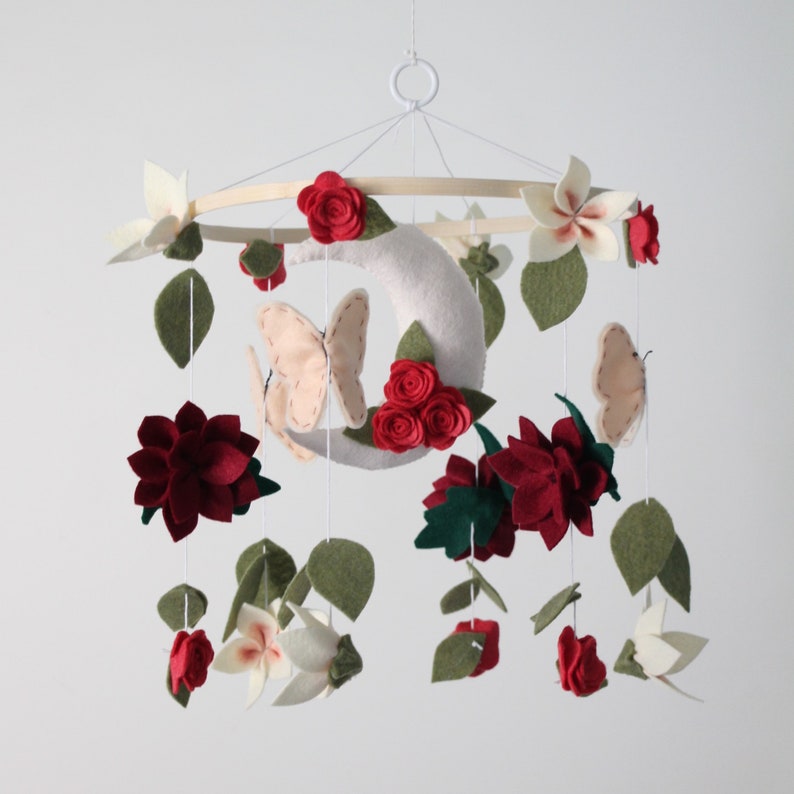 Mobile with light pink butterflies, red roses, burgundy dahlias, and white pink centered cherry blossoms hang off a bamboo hoop with a white crescent moon with three red roses in the middle.