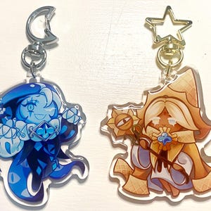 May include: Two acrylic keychains featuring cartoon characters. One is blue with a crescent moon clasp, the other is tan with a star clasp. The characters have detailed designs and are attached to silver-colored keychains.