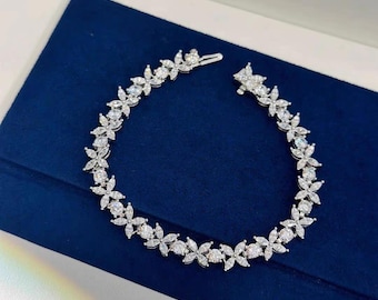 May include: A delicate silver bracelet with a floral design, featuring a row of sparkling diamonds set in a flower shape.