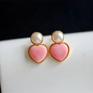May include: A pair of gold heart-shaped earrings with pink centers and white pearl accents.