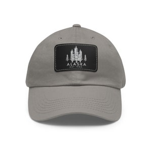 May include: A gray baseball cap with a black patch featuring a white outline of trees and the text "ALASKA EST. 1959".