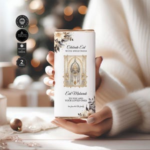 Puede incluir: Una caja de regalo rectangular blanca con detalles florales y de hojas, con el texto "Celebrate Eid with Sweetness" y "Eid Mubarak". El diseño incluye una ilustración de una mezquita. La caja está sostenida en las manos de una persona.