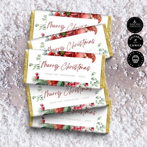 Może przedstawiać: Opakowania czekoladowych batonów ze złotą folią i białą etykietą. Na etykiecie napis "Merry Christmas" w ozdobnej czcionce, z napisem "From The Fergusons - 2023" poniżej. Opakowania zdobią akwarelowe ilustracje czerwonych jagód i zielonych liści.