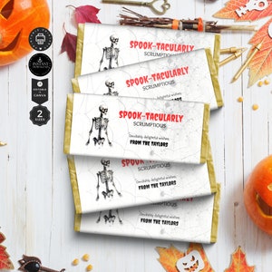 May include: Halloween-themed candy bar wrappers with a skeleton graphic and the words "SPOOK-TACULARLY SCRUMPTIOUS." The wrappers have a white background with a spiderweb design and gold edges. The text "FROM THE TAYLORS" is also included.