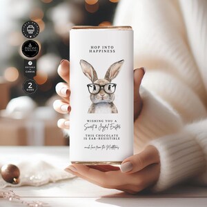May include: A white chocolate bar wrapper with a bunny wearing glasses. The text on the wrapper reads "Hop into happiness. Wishing you a Sweet & Joyful Easter. This chocolate is ear-resistible. Much love from the Maddens."