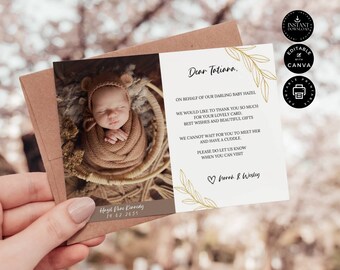 May include: A baby announcement card held by a hand. The card features a photo of a newborn baby wrapped in a brown blanket and wearing a bear hat. Text includes a thank you message, names, and a date.