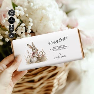 May include: A white chocolate bar wrapper with a bunny rabbit illustration holding a basket of Easter eggs. The wrapper has the text "Hoppy Easter" and "Wishing you a sweet and joyful celebration!" with a heart and "from The Smiths".