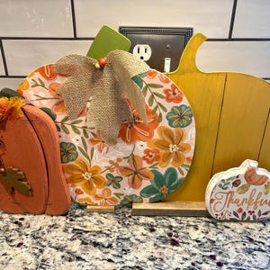 May include: A set of four decorative wooden pumpkin cutouts. One is orange with a leaf accent, one is round with a floral pattern and burlap leaf, one is a large yellow pumpkin, and one is a small white pumpkin with the text Thankful.