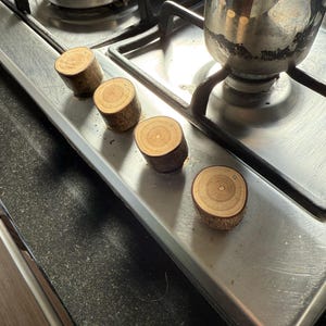 May include: Four wooden knobs of varying sizes and shades of brown are arranged in a row on a stainless steel hob. The knobs are crafted from natural wood and have a rustic appearance.
