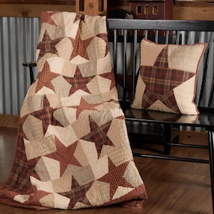 May include: A quilted throw blanket and pillow set featuring a star pattern. The blanket and pillow have a patchwork design with red, tan, and cream-colored fabrics. The star shapes are prominently displayed against a neutral background, creating a rustic, country aesthetic.