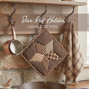 Puede incluir: Un salvamanteles acolchado con forma de estrella en marrón y beige con un paño de cocina a cuadros a juego colgando de un estante de madera. El salvamanteles es 100% algodón y presenta un diseño de estrella. Una taza medidora de cobre cuelga a la izquierda.