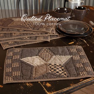 May include: Quilted placemats made of 100% cotton. The placemats feature a star design in the center, surrounded by a checkered pattern. The color scheme includes shades of brown and cream. The text "Quilted Placemat" and "100% Cotton" are visible.