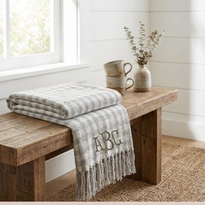 May include: A white ceramic mug with a black handle and the text "But First, Coffee" in a bold, black font. The mug is set against a blurred background, highlighting its clean design.