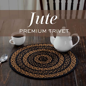 May include: A round, braided jute trivet featuring alternating concentric circles of natural tan and black fibers. The text Jute PREMIUM TRIVET is overlaid on the image. The trivet is displayed on a dark wooden surface with a white teapot and cup.
