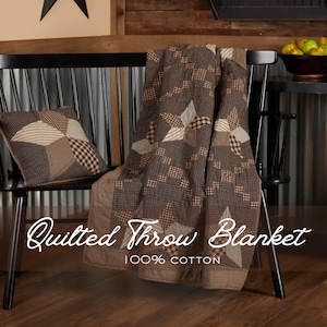 May include: A brown and tan quilted throw blanket and matching pillow with star and square patterns, draped over a black chair. The blanket is made of 100% cotton. The words "Quilted Throw Blanket" are written on the blanket.