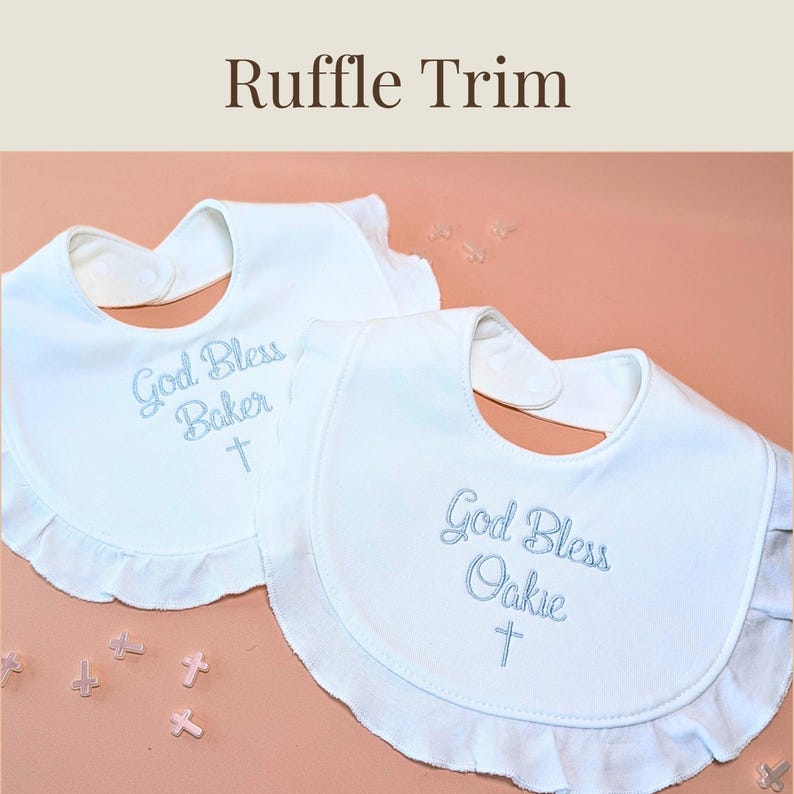 two white ruffled bibs with embroidered text, placed on a peach-colored background.