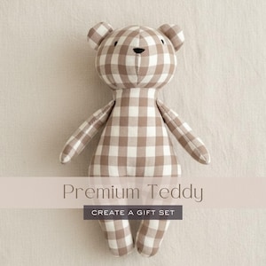 Può includere: Un orsacchiotto di peluche con un motivo a quadretti vichy marrone e bianco. Il giocattolo ha piccole orecchie arrotondate, un semplice naso nero ricamato e due piccoli occhi neri. Il testo Premium Teddy CREATE A GIFT SET è sovrapposto all'immagine.