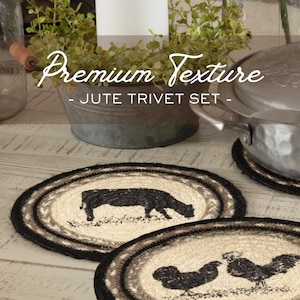 May include: Oval jute trivet set with a black and cream color scheme. The trivets feature a black border, a cream-colored center, and a brown and cream patterned design. One trivet has a black cow silhouette, and the other has two black rooster silhouettes. The text "Premium Texture - Jute Trivet Set -" is visible.